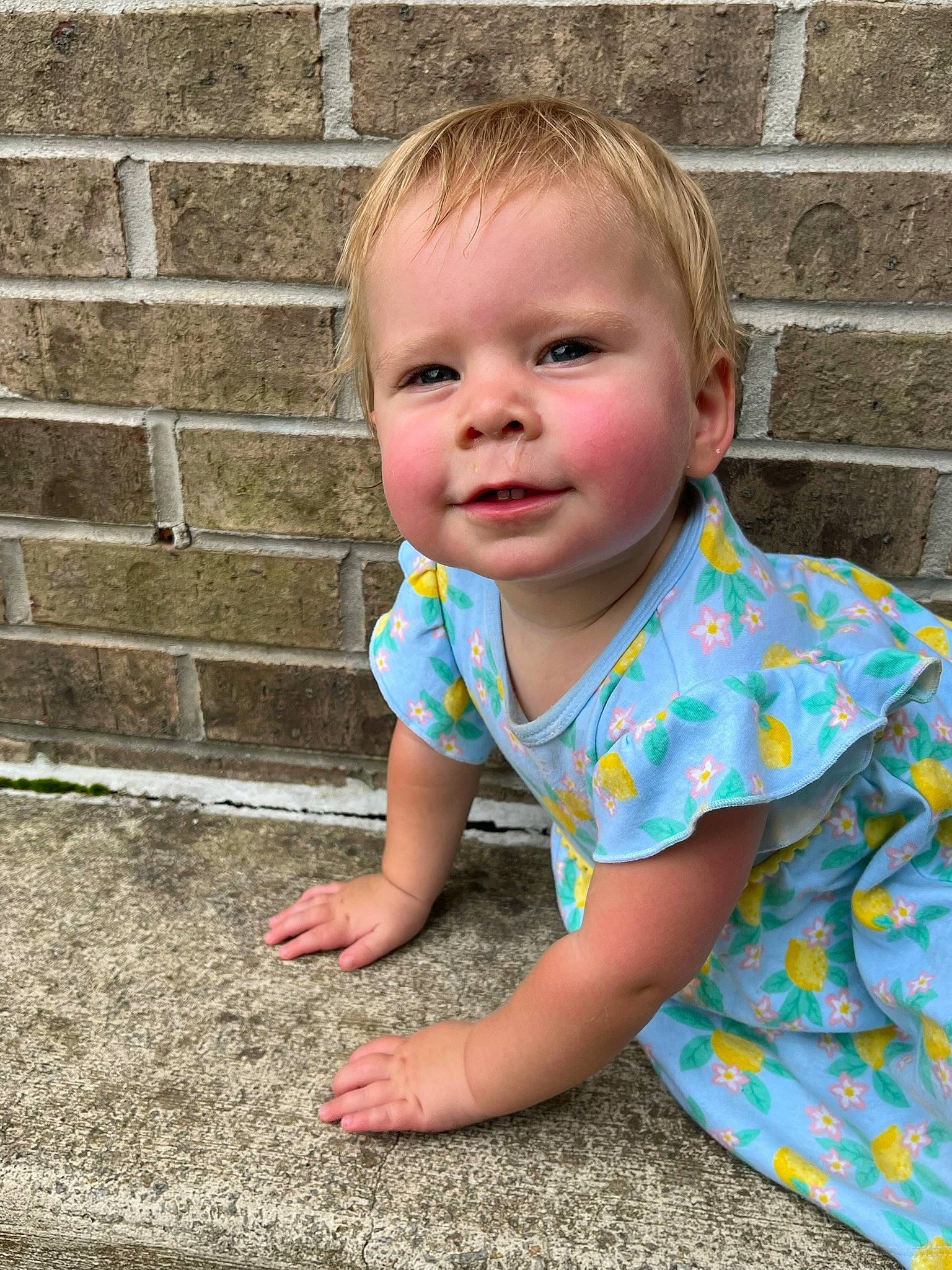Emerald is registered to the contest to win money with this photo: baby, baby_toddler_clothing, brickwork, cheek, chin, eye, flooring, fun, grass, happy, head, pattern, person, road_surface, skin, smile, standing, t_shirt, toddler, tree