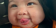 Areli is registered to the contest to win money with this photo: baby, face, tongue, orange_shirt, car_seat, black_straps, child, cute, chubby_cheeks, expression, infant, young_child, portrait, smile, closeup, seatbelt, safety, indoors, hair_tie, person
