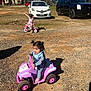 Areli joined the competition — help win amazing prizes! child, toddler, toy_vehicle, quad_bike, tricycle, outdoor, sunny, gravel, dirt, play, fun, vehicle, car, parked_car, shadow, grass, tree, person, clothing, happy