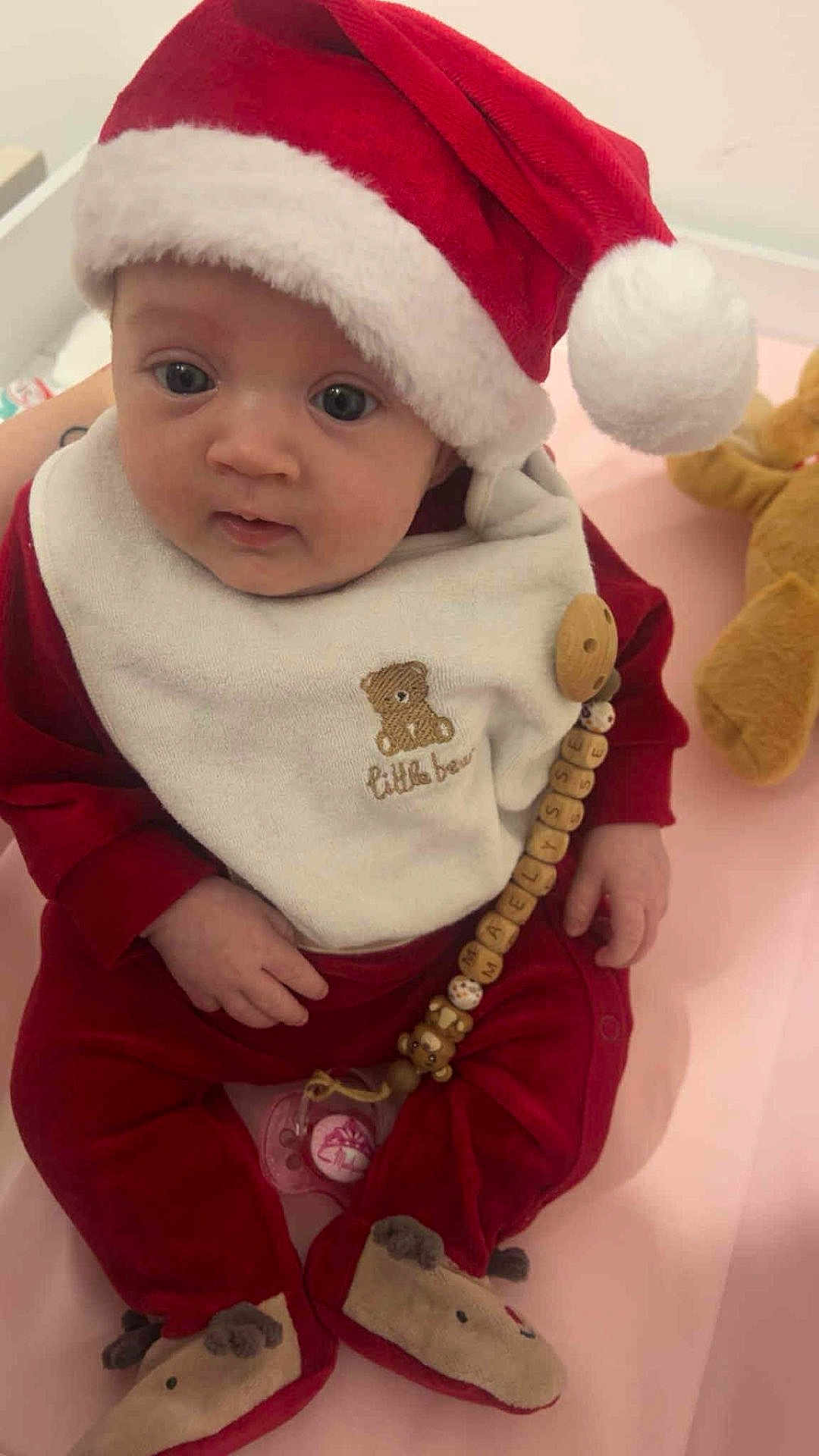 Maëlysse a rejoint le concours — aidez-le/la à gagner de superbes lots ! baby, infant, santa_hat, red_clothing, bib, pacifier, pacifier_clip, plush_toy, teddy_bear, indoors, child, cute, holiday, christmas, soft_toy, person, sitting, face, headwear, cozy