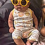 baby, child, sunglasses, yellow, romper, animal_print, sitting, cushion, indoor, cute, chubby, footwearless, plush, clothing, face, head, infant, portrait, funny, accessory