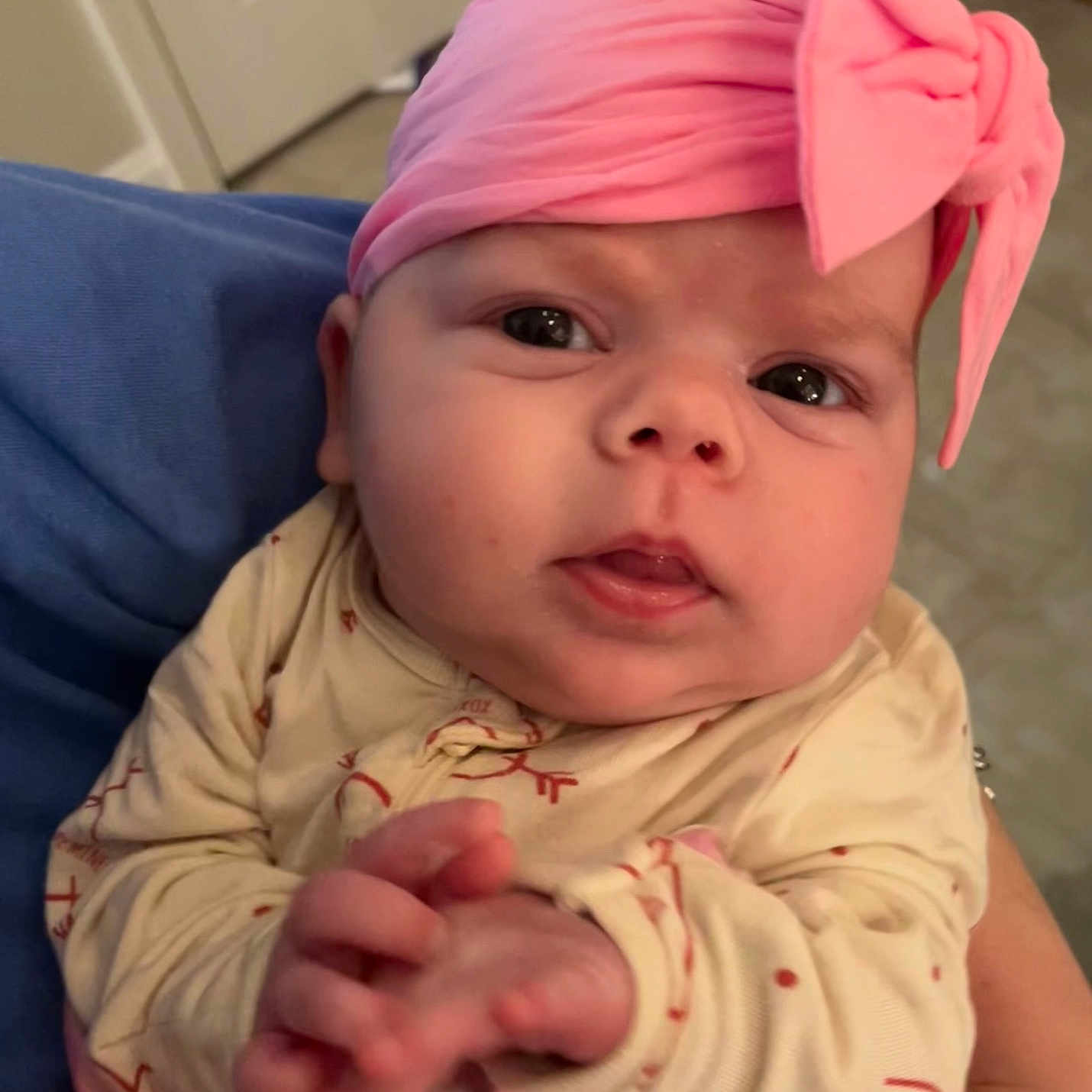 Kayla is registered to the contest to win money with this photo: baby, infant, headband, pink, bow, clothing, hands, face, eyes, indoor, person, cute, newborn, expression, portrait, closeup, holding, human, child, soft