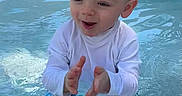 Cadence joined the competition — help win amazing prizes! toddler, child, pool, water, clapping, happy, sitting, swimwear, white_shirt, blue_trunks, outdoor, sunlight, playful, toy_ball, shallow_water, summer, fun, cute, excited, smiling
