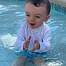toddler, child, pool, water, clapping, happy, sitting, swimwear, white_shirt, blue_trunks, outdoor, sunlight, playful, toy_ball, shallow_water, summer, fun, cute, excited, smiling
