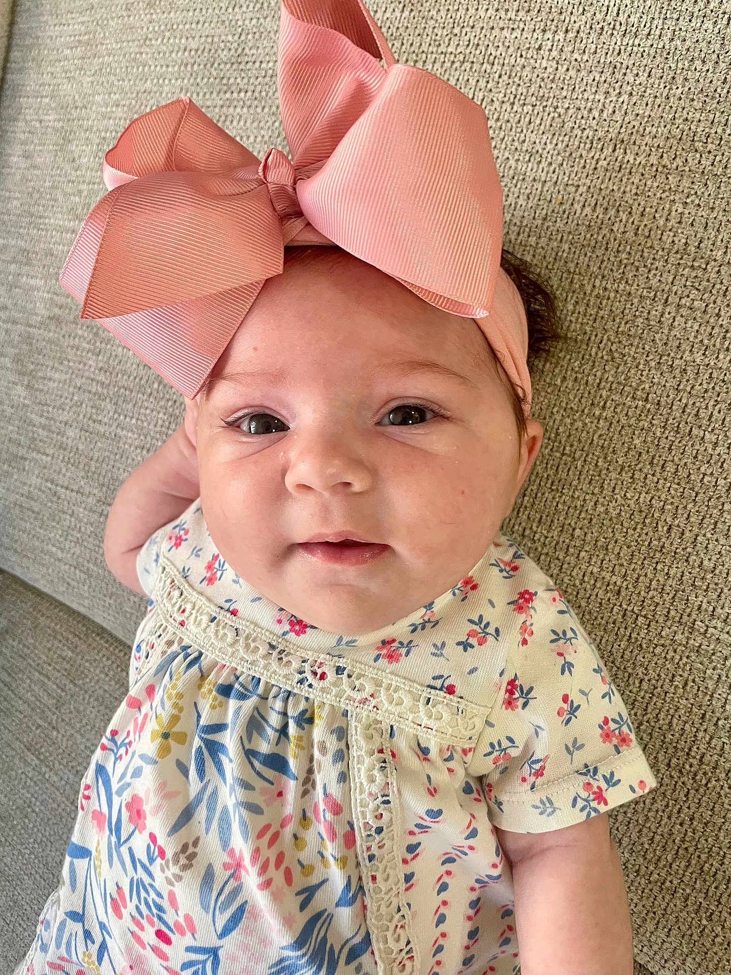 Aria a rejoint le concours — aidez-le/la à gagner de superbes lots ! baby, infant, child, headband, bow, pink, floral_dress, couch, textured_fabric, face, eyes, cute, portrait, closeup, smile, skin, hand, lying_down, indoors, soft_lighting