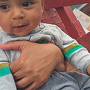 Maddox joined the competition — help win amazing prizes! child, toddler, face, hand, curly_hair, sweater, colorful_stripes, skin, outdoor, brick_wall, railing, person, cute, portrait, baby, holding, casual_clothing, expression, closeup, natural_light