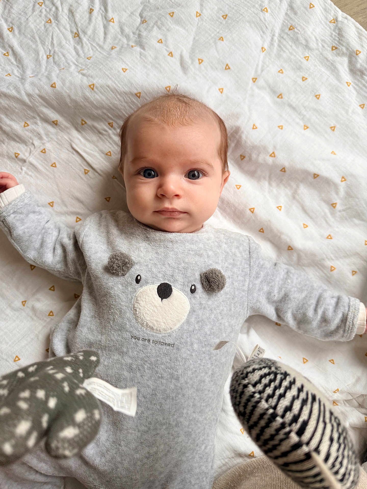 Camille a rejoint le concours — aidez-le/la à gagner de superbes lots ! baby, infant, onesie, bear_design, blanket, toy, soft_texture, curious_expression, lying_down, indoor, child, cute, cozy, patterned_blanket, blue_eyes, small_hands, plush_toy, comfortable, portrait, young