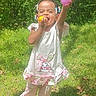 Camila is registered to the contest to win money with this photo: bunny_dress, child, colorful_beads, cute, garden, grass, greenery, happy, nature, outdoors, pink_clothing, playtime, portrait, purple_ball, smiling, standing, sunlight, toddler, toy, trees