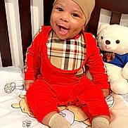 Jasai joined the competition — help win amazing prizes! baby, child, smiling, happy, portrait, sitting, crib, teddy_bear, stuffed_animal, red_outfit, beanie, bib, blanket, bedroom, nursery, indoor, face, eyes, teeth, playful