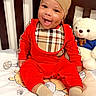 baby, child, smiling, happy, portrait, sitting, crib, teddy_bear, stuffed_animal, red_outfit, beanie, bib, blanket, bedroom, nursery, indoor, face, eyes, teeth, playful