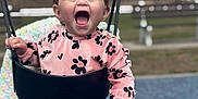 Raziella is registered to the contest to win money with this photo: toddler, child, swing, playground, pink_outfit, flower_pattern, happy, smiling, outdoor, bench, chain, grass, trees, face, person, clothing, joy, fun, baby, seat