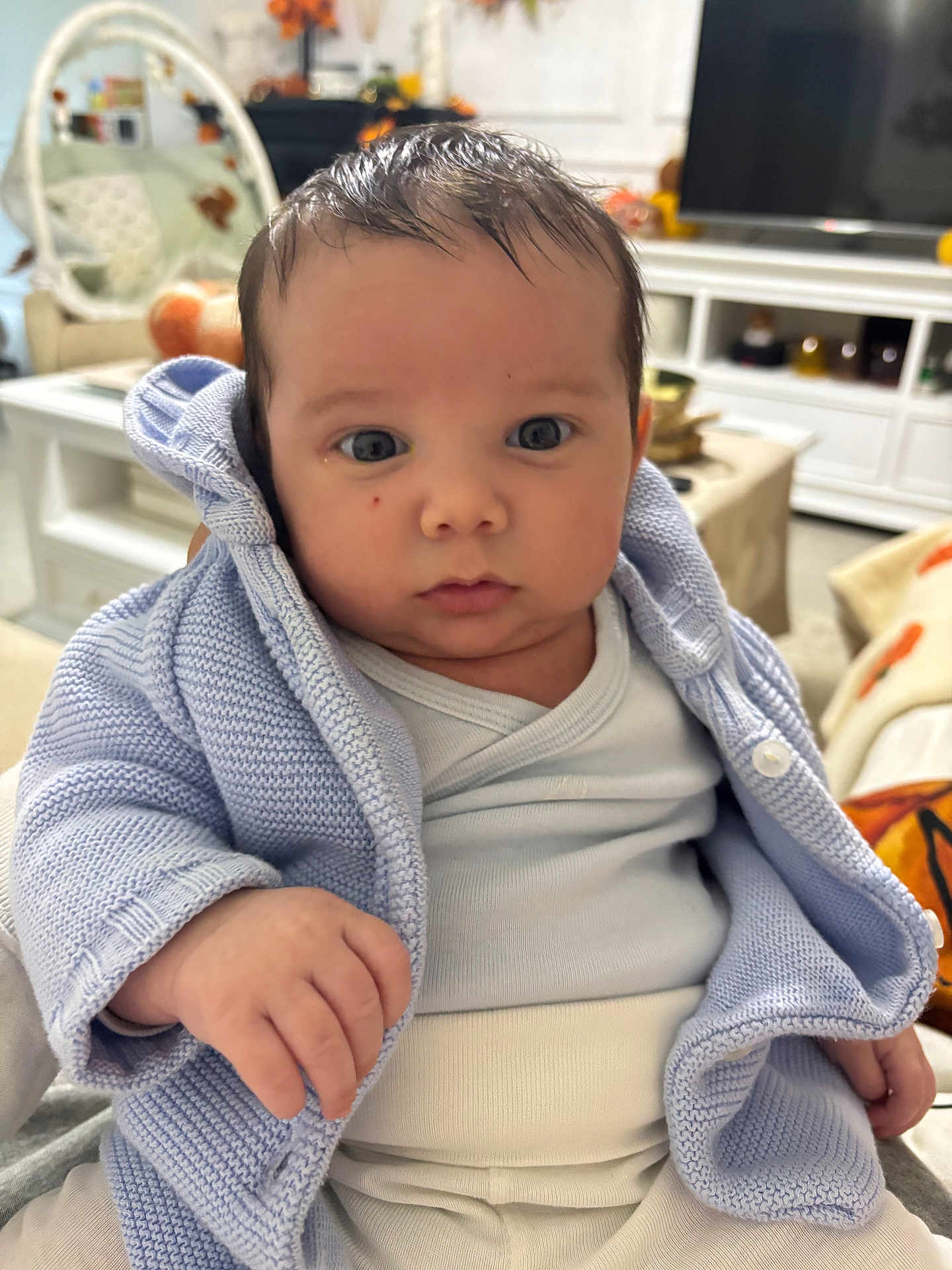 élio a rejoint le concours — aidez-le/la à gagner de superbes lots ! baby, infant, child, blue_jacket, white_onesie, face, hand, indoor, furniture, television, knitwear, curious, portrait, person, home, decor, soft_lighting, closeup, cute, young