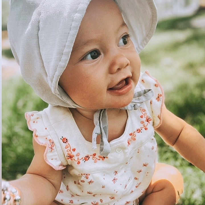 Roxiana is registered to the contest to win money with this photo: baby, babylaughing, baseballcap, bonnet, cap, clothing, dress, face, grass, happy, hat, head, hood, person, photography, plant, portrait, sitting, smile, sunhat