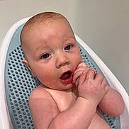 Archie is registered to the contest to win money with this photo: baby, child, bath, bathtub, blue_bath_seat, skin, wet, hands, face, curious, infant, person, cute, water, clean, indoor, plump, expression, young, naked