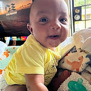 Tynan is registered to the contest to win money with this photo: baby, child, infant, smiling, happy, portrait, yellow_outfit, sitting, blanket, plush_toy, pacifier, toy, bedroom, indoors, window, television, home, sunlight, close_up, face