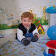 Gabriel joined the competition — help win amazing prizes! toddler, child, smiling, sitting, toy, balloon, blanket, indoor, playtime, cute, happy, face, clothing, jeans, jacket, background, decor, animal_print, colorful, room