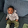 toddler, child, couch, clothing, hoodie, pants, sneakers, footwear, curly_hair, indoor, furniture, seated, young_child, expression, face, person, textile, cushion, blanket, casual_wear