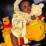 baby, child, plush_toy, winnie_the_pooh, stuffed_animal, yellow_robe, slippers, indoor, black_leather_chair, cute, soft_toy, childrens_toy, smiling, happy, cozy, person, infant, face, seated, warm_clothing