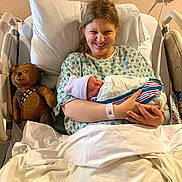 Michael joined the competition — help win amazing prizes! newborn, baby, mother, hospital_bed, hospital_gown, teddy_bear, chewbacca_toy, smile, woman, bed, blanket, swaddle, hospital_room, medical_device, face, person, comfort, happy, indoor, family