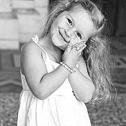 Léna participe au concours pour gagner de l'argent avec cette photo : child, girl, portrait, smile, curly_hair, hair_clip, white_dress, bracelet, ring, playful_pose, cute, standing, face, eyes, hands, long_hair, black_and_white, architecture, stone_floor, outdoor