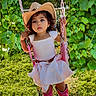 child, girl, swing, cowboy_hat, dress, pink, outdoor, greenery, grass, playground, curly_hair, portrait, summer, nature, cute, boots, holding_chains, sunlight, young, daytime