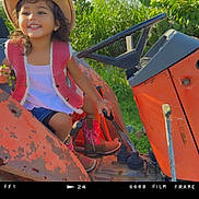 Malia joined the competition — help win amazing prizes! child, girl, cowboy_hat, pink_vest, boots, tractor, rusty, outdoor, greenery, grass, smile, happy, sunlight, nature, playful, farm, vehicle, seat, hand, young