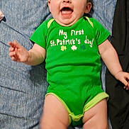 Eve joined the competition — help win amazing prizes! baby, child, infant, onesie, green_clothing, st_patrick, smiling, laughing, lying_down, blue_sheet, bed, chubby_legs, hands, face, hair, portrait, indoor, cute, happy, clothing