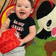 Eve joined the competition — help win amazing prizes! baby, black_shirt, carpet, child, colorful, cute, happy, indoor, infant, joyful, lying_down, panda, person, playful, red_block, smiling, soft_toy, text_on_clothing, toy, young_child
