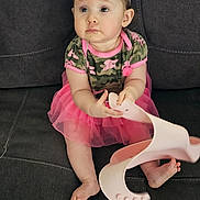 Eve is registered to the contest to win money with this photo: baby, bow, camouflage, casual, child, clothing, couch, cute, expression, footwear, furniture, girl, home, indoor, person, pink, sandal, sitting, sofa, toddler