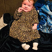 Eve is registered to the contest to win money with this photo: baby, blanket, child, couch, cozy, cute, dress, face, furniture, happy, head, home, indoor, infant, leopard_print, person, plush, sitting, smile, socks