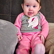Eve is registered to the contest to win money with this photo: baby, infant, child, unicorn, pajamas, pink, couch, sofa, pillow, socks, feet, smile, face, eyes, hair, hand, indoor, portrait, living_room, cute