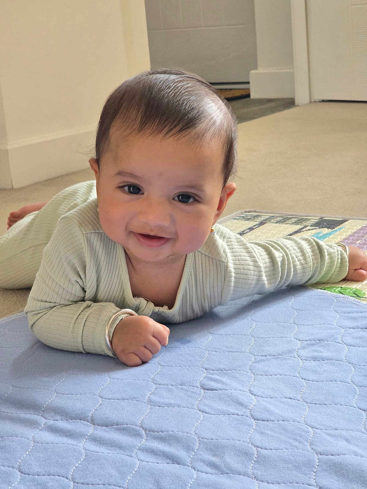 Avyaan joined the competition — help win amazing prizes! baby, smiling, indoor, floor, blue_quilt, bracelet, infant, person, cute, tummy_time, carpet, child, portrait, happy, young, head, hand, cozy, home, clothing
