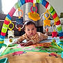 baby, play_mat, colorful_toys, baby_gym, living_room, curtains, sofa, carpet, child, infant, floor_play, indoor, cute, colorful, toy_arch, onesie, toddler, furniture, bright, happy