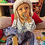 toddler, child, pacifier, hat, pajamas, blanket, toy, indoor, blue_eyes, face, cute, infant, clothing, soft, beads, seat, expression, looking_up, warm_lighting, home