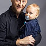 man, baby, child, pacifier, beard, smile, portrait, holding, casual_clothing, watch, indoor, studio, blue_eyes, blond_hair, adult, parent, affection, family, closeup, gentle