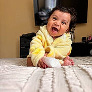 Carlos joined the competition — help win amazing prizes! baby, smiling, yellow_robe, indoor, bed, bottle, curly_hair, happy, face, child, person, room, television, furniture, blanket, foot, hand, portrait, cute, cozy