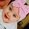 baby, baby_girl, blue_eyes, child, closeup, cute, drool, face, happy, headband, headwear, indoor, infant, person, pink_bow, portrait, smile, white_clothing, woman_partial, young_child