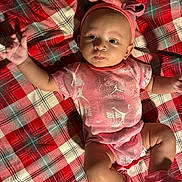 Zaryiah is registered to the contest to win money with this photo: baby, infant, child, portrait, lying_down, pink_outfit, headband, bow, socks, plaid_blanket, red_blanket, indoor, close_up, face, eyes, arms_raised, smiling, fashion, textured_fabric, cute