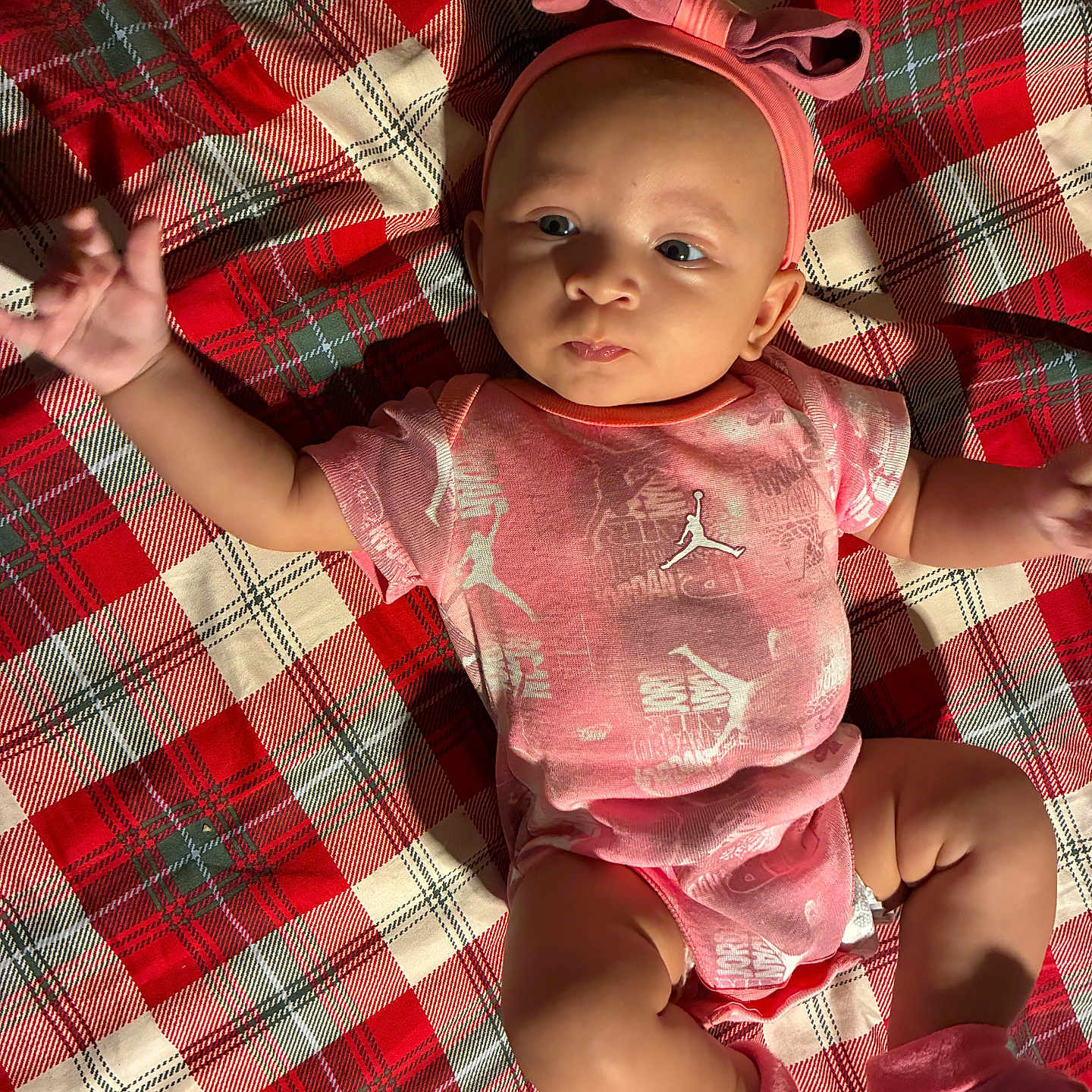 Zaryiah is registered to the contest to win money with this photo: baby, infant, child, portrait, lying_down, pink_outfit, headband, bow, socks, plaid_blanket, red_blanket, indoor, close_up, face, eyes, arms_raised, smiling, fashion, textured_fabric, cute