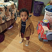 Ocean joined the competition — help win amazing prizes! child, toddler, portrait, standing, indoors, home, living_room, coat, boots, curly_hair, face, person, toy_car, laundry_basket, bed, blanket, television, wooden_floor, fashion, cute