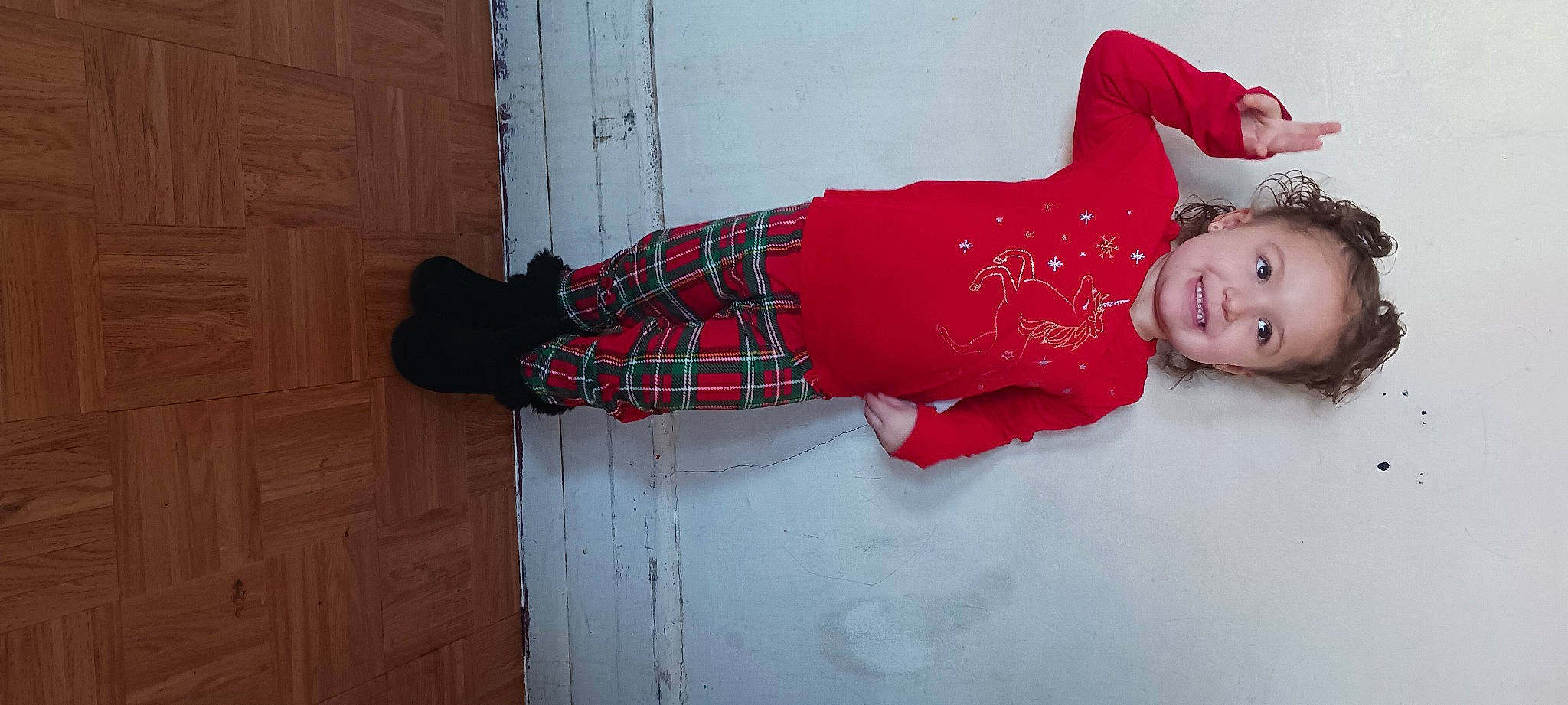 Isabella is registered to the contest to win money with this photo: baby_toddler_clothing, carmine, child, door, flooring, fun, happy, human_leg, joy, knee, magenta, pattern, person, plaid, red, sitting, sleeve, smile, sock, tartan