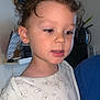 child, curly_hair, white_shirt, duck_print, face, portrait, young_child, indoor, kitchen, painting, appliance, expression, calm, person, clothing, young, toddler, curly, casual, home