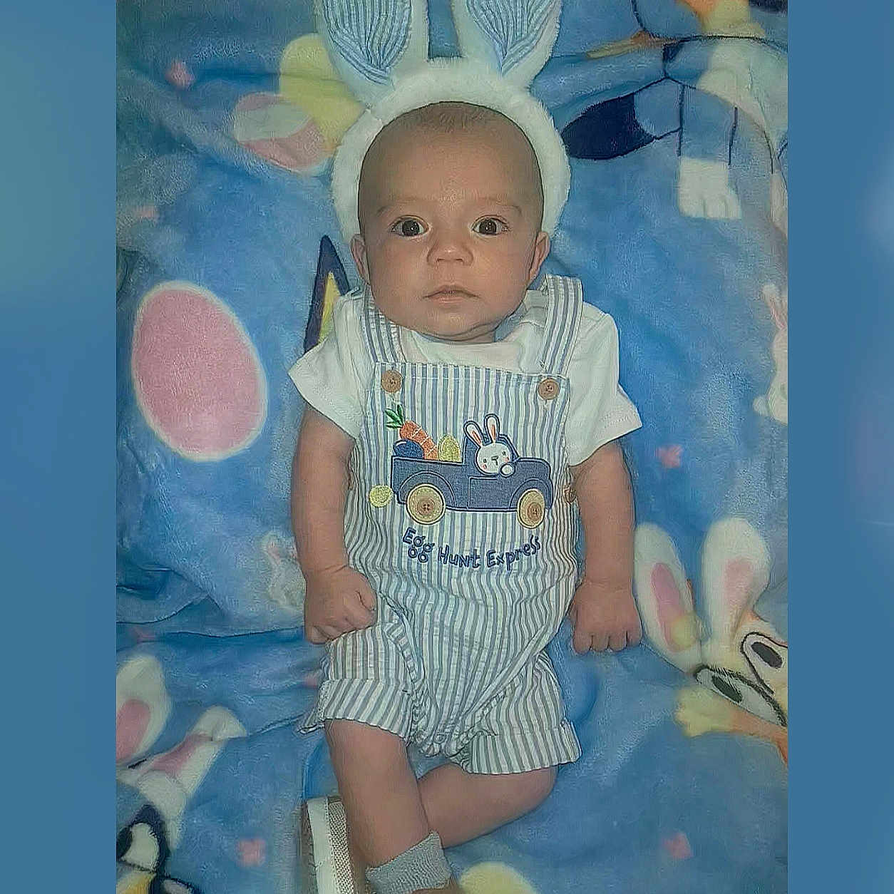 Zarin is registered to the contest to win money with this photo: baby, infant, child, bunny_ears, overalls, striped_clothing, blue_blanket, cartoon_pattern, toy, cute, portrait, indoor, lying_down, headgear, expression, small_hands, footwear, sock, animal_theme, soft_texture