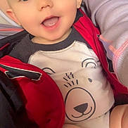 Jaxzon is registered to the contest to win money with this photo: baby, child, smiling, face, eyes, mouth, clothing, jacket, red, white, bear_design, person, arm, hand, closeup, infant, cute, happy, indoors, portrait