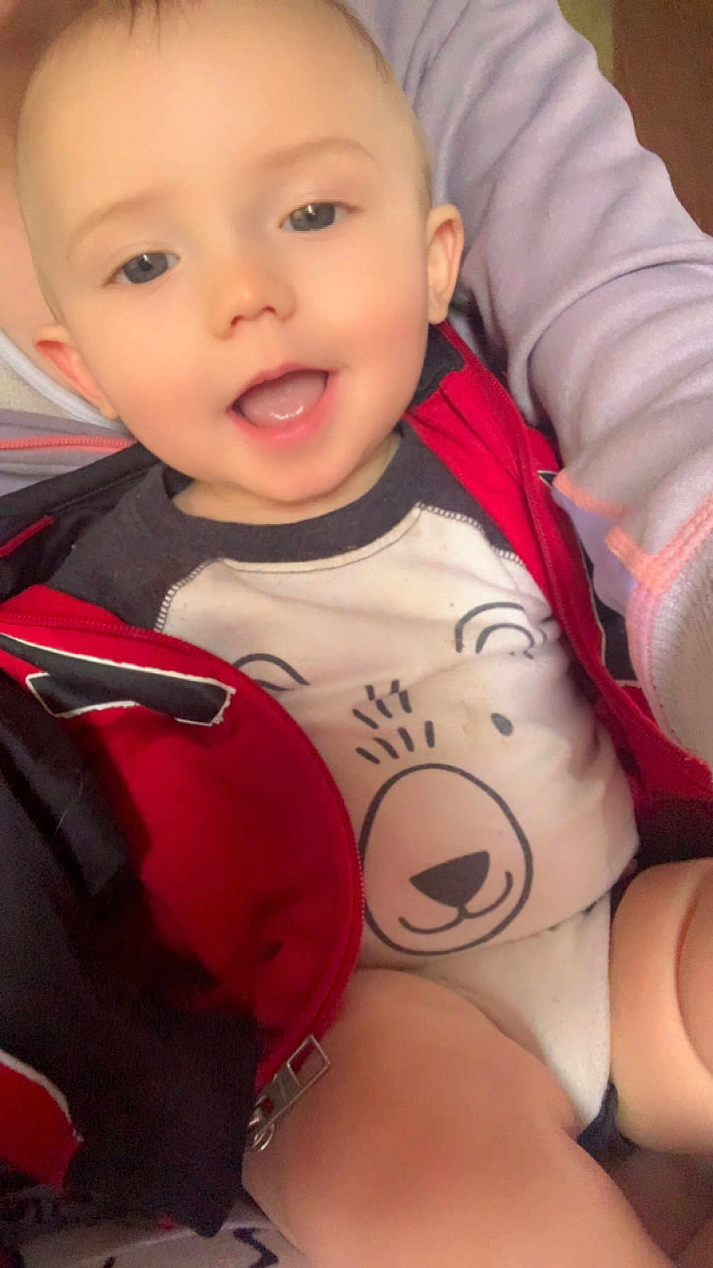 Jaxzon is registered to the contest to win money with this photo: baby, child, smiling, face, eyes, mouth, clothing, jacket, red, white, bear_design, person, arm, hand, closeup, infant, cute, happy, indoors, portrait