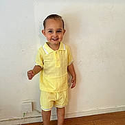 Sandro participe au concours pour gagner de l'argent avec cette photo : toddler, child, smiling, yellow_clothing, shorts, shirt, barefoot, wooden_floor, indoor, wall, hair, happy, standing, person, cute, casual, portrait, light, young, feet