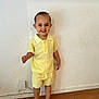 toddler, child, smiling, yellow_clothing, shorts, shirt, barefoot, wooden_floor, indoor, wall, hair, happy, standing, person, cute, casual, portrait, light, young, feet