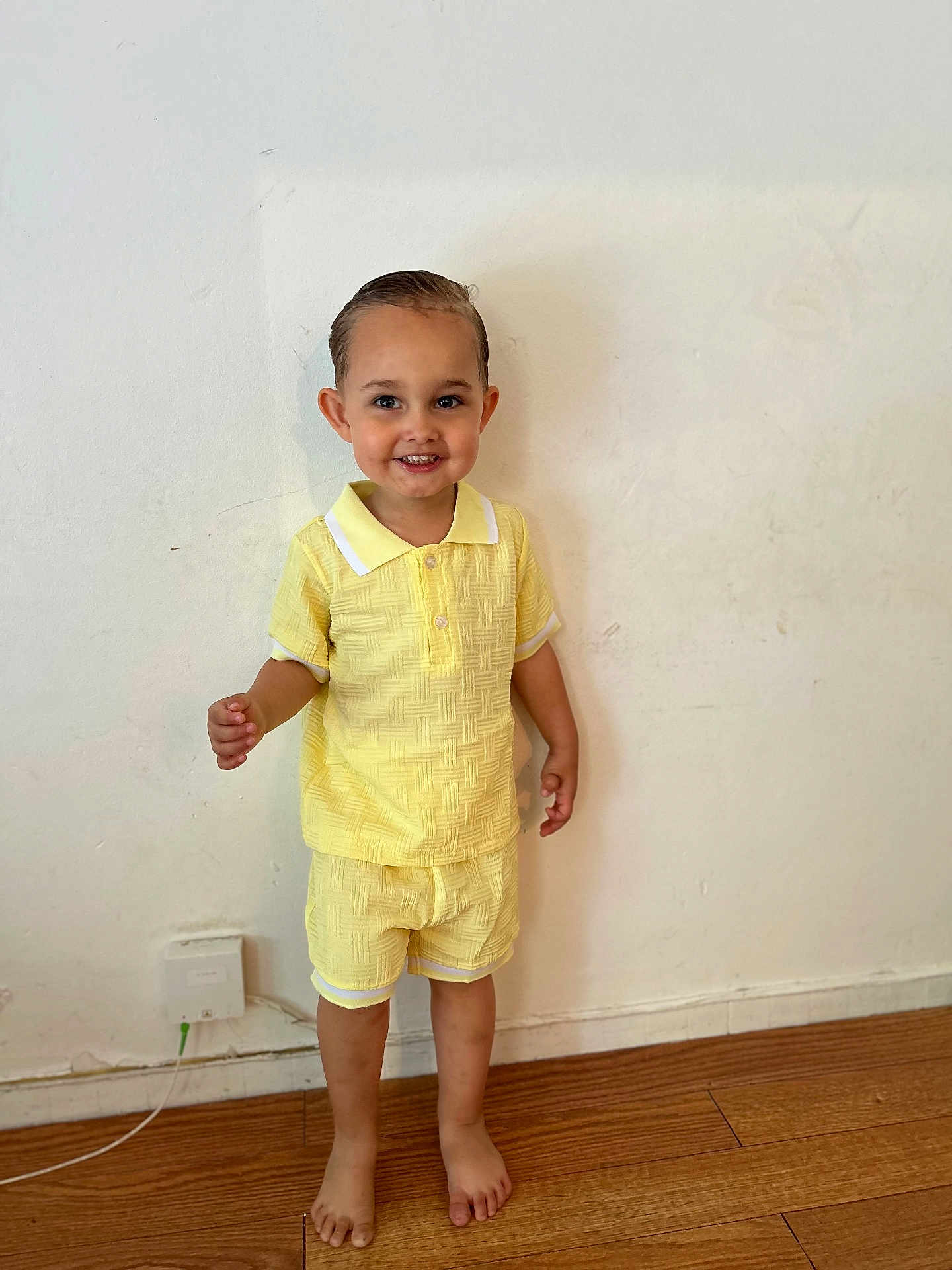 Sandro participe au concours pour gagner de l'argent avec cette photo : toddler, child, smiling, yellow_clothing, shorts, shirt, barefoot, wooden_floor, indoor, wall, hair, happy, standing, person, cute, casual, portrait, light, young, feet