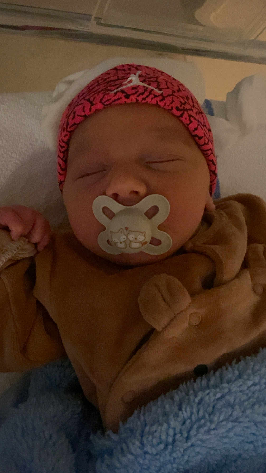 Lyam participe au concours pour gagner de l'argent avec cette photo : baby, newborn, infant, pacifier, sleeping, hat, pink_hat, blanket, blue_blanket, onesie, brown_clothing, face, cheeks, closed_eyes, hand, cozy, portrait, crib, soft_texture, cute