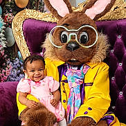 Kmiyah joined the competition — help win amazing prizes! child, toddler, costume, bunny, mascot, purple_throne, glasses, yellow_jacket, pink_dress, smile, flowers, background, indoor, portrait, happy, person, cute, seated, holiday, celebration